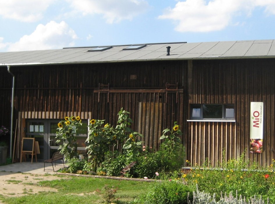 Holzfassade eines Bauernhofgebäudes mit Sonnenblumen und einem Schild mit der Aufschrift MiO